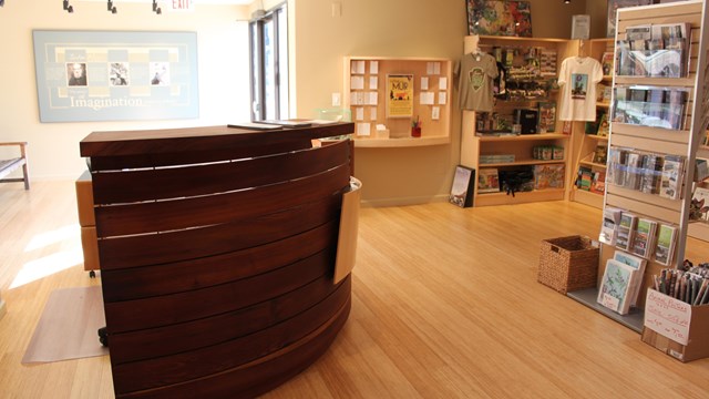 A tall front desk for sales with bookshelves in the background. Lots of books, and objects. 